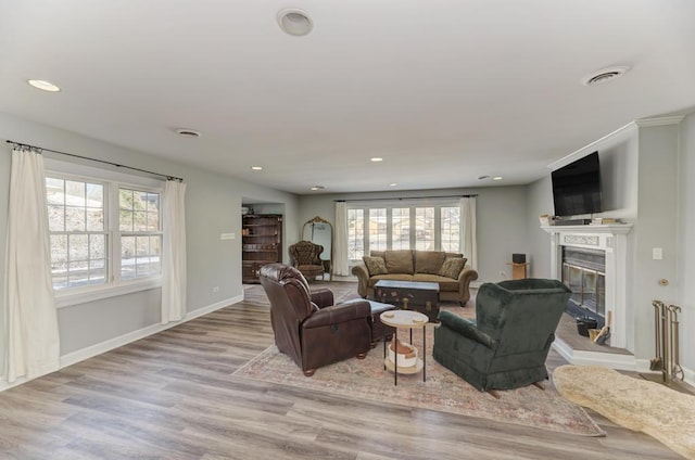 living room with a glass covered fireplace, plenty of natural light, visible vents, and wood finished floors