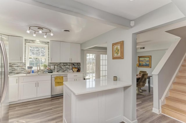 kitchen featuring light wood finished floors, stainless steel appliances, light countertops, a sink, and decorative backsplash