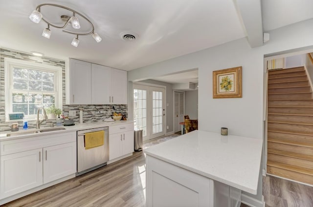 kitchen with a sink, white cabinets, dishwasher, light wood-style flooring, and backsplash