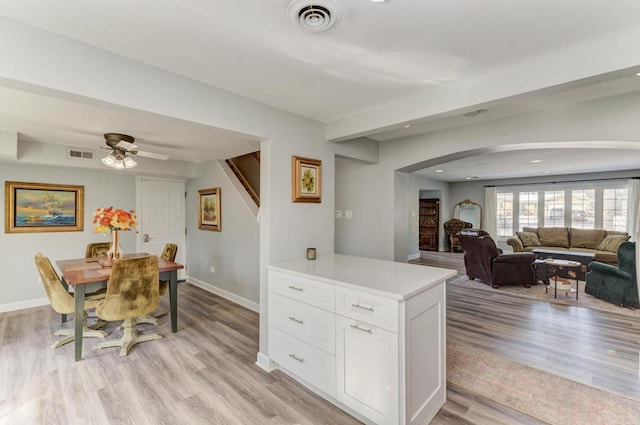 kitchen with arched walkways, light wood-style floors, visible vents, and white cabinets