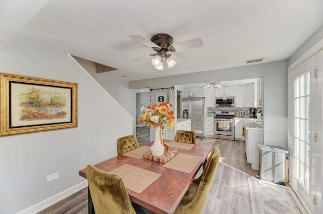 dining room featuring visible vents, a ceiling fan, light wood-style floors, baseboards, and stairs