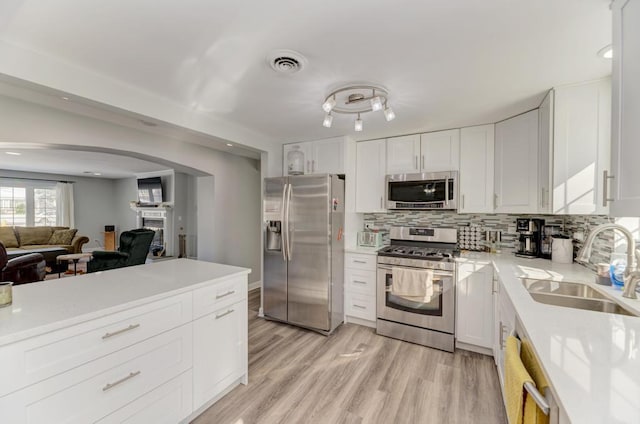 kitchen with a sink, arched walkways, stainless steel appliances, light countertops, and white cabinetry