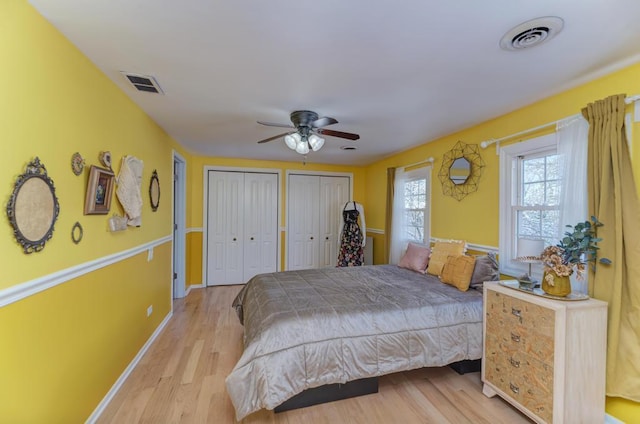 bedroom with two closets, a ceiling fan, visible vents, and light wood-type flooring