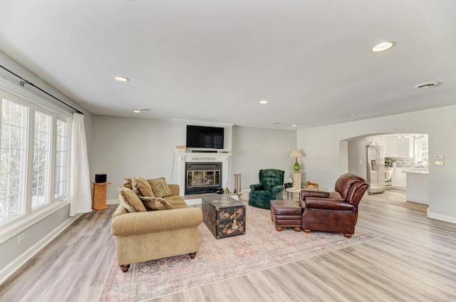 living area featuring recessed lighting, a glass covered fireplace, arched walkways, and light wood-style floors