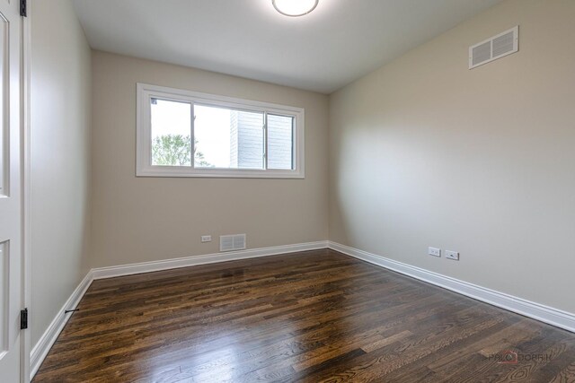 empty room featuring dark wood-style flooring, baseboards, and visible vents