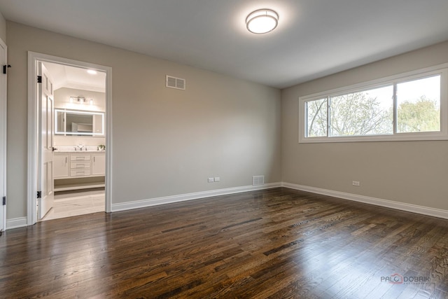 empty room featuring dark wood-style flooring, baseboards, and visible vents