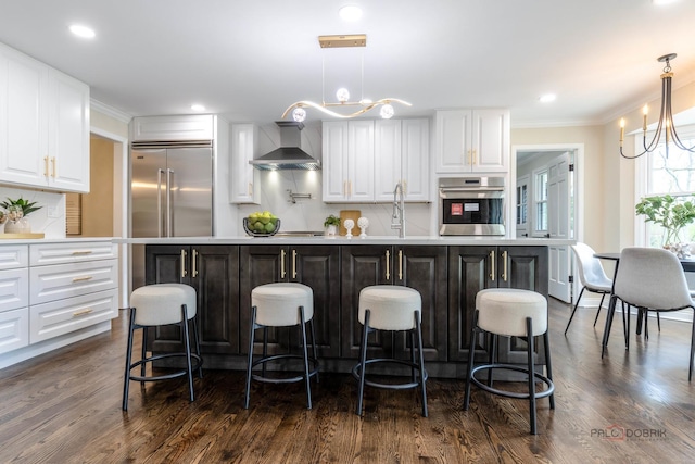 kitchen featuring wall chimney range hood, appliances with stainless steel finishes, an inviting chandelier, and tasteful backsplash