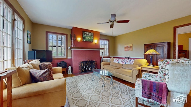 living room with wood finished floors, ceiling fan, and a brick fireplace
