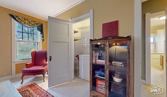 sitting room with baseboards, stacked washing maching and dryer, ornamental molding, and carpet flooring