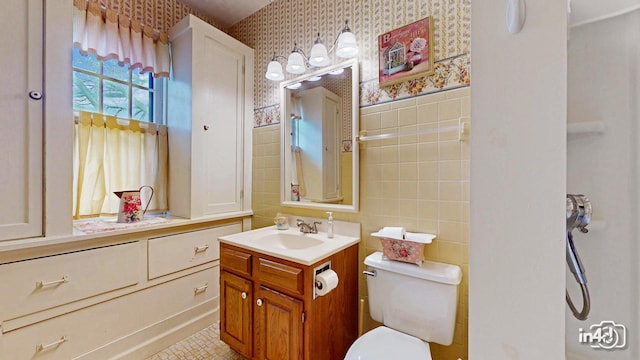bathroom featuring a wainscoted wall, wallpapered walls, toilet, tile walls, and vanity