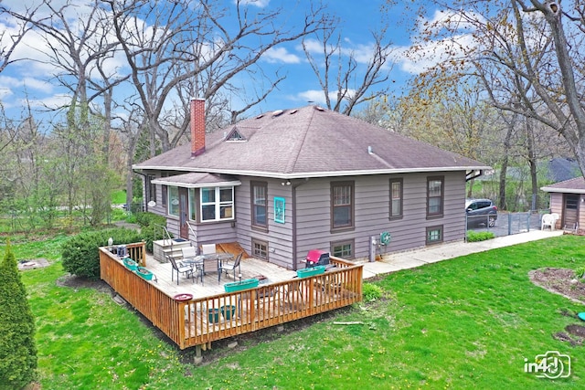 back of house with a chimney, roof with shingles, a wooden deck, and a lawn