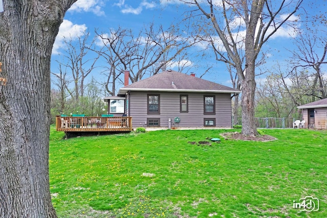 back of house featuring a chimney, a deck, a shingled roof, fence, and a yard