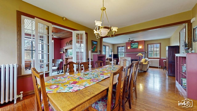 dining space with radiator, wood finished floors, and ceiling fan with notable chandelier