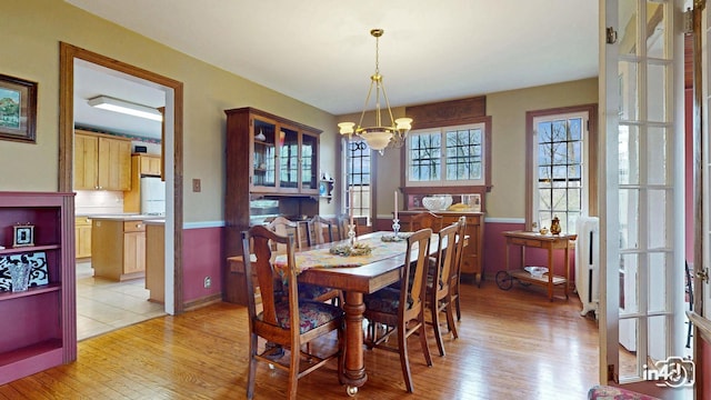 dining space with an inviting chandelier, baseboards, light wood-style flooring, and wainscoting