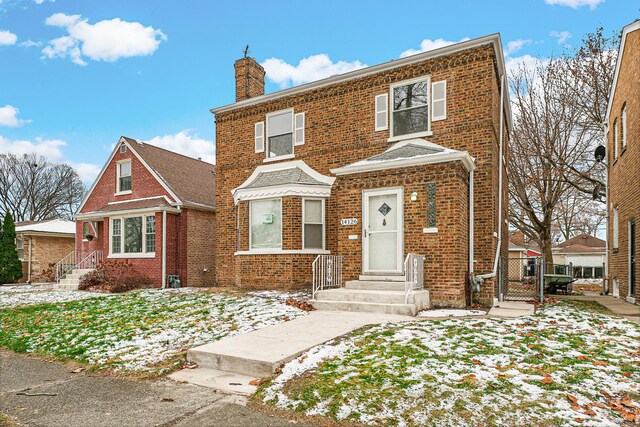 view of front of home featuring a chimney, brick siding, and a gate