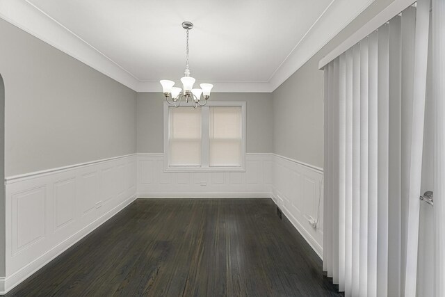 empty room featuring dark wood-type flooring, wainscoting, ornamental molding, and an inviting chandelier