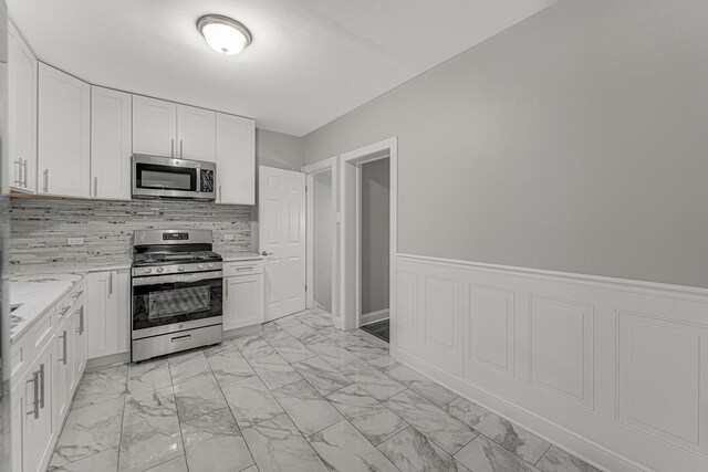 kitchen with marble finish floor, light stone counters, stainless steel appliances, tasteful backsplash, and white cabinetry