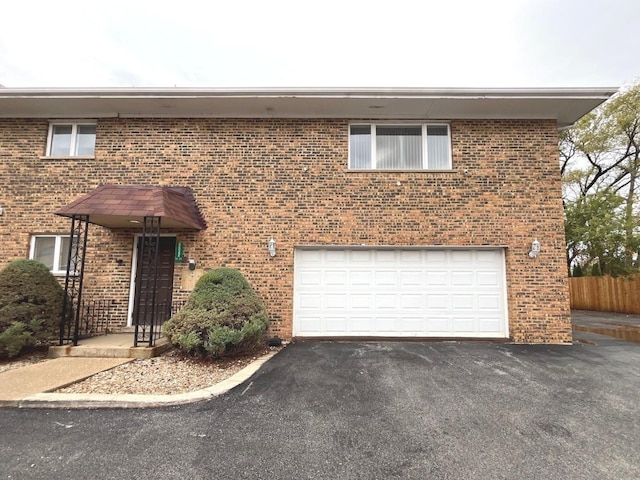view of front of house featuring brick siding, an attached garage, driveway, and fence