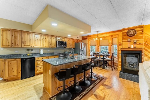 kitchen with light wood finished floors, an island with sink, a breakfast bar, a sink, and appliances with stainless steel finishes