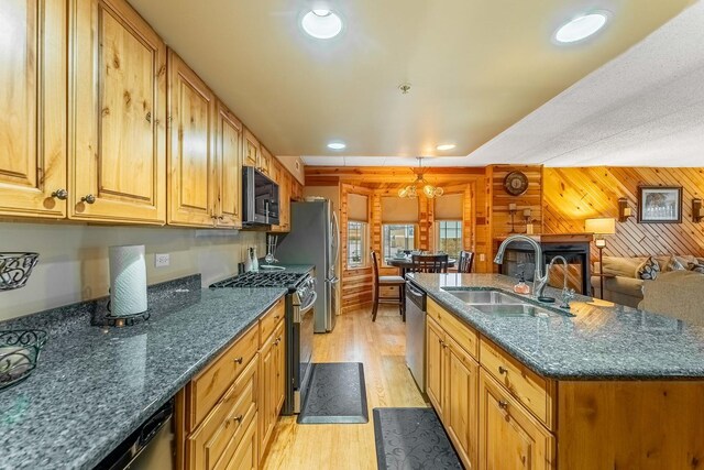kitchen with a sink, light wood-style floors, wood walls, an island with sink, and appliances with stainless steel finishes