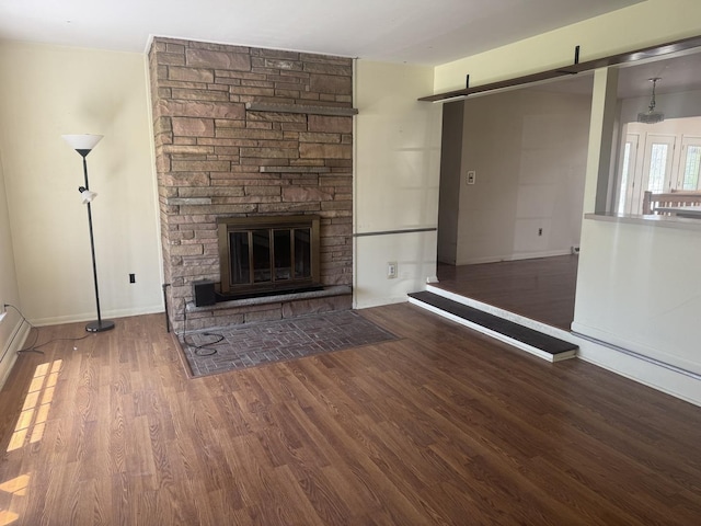 unfurnished living room featuring a stone fireplace, a barn door, baseboards, and wood finished floors