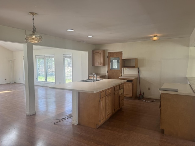 kitchen featuring a sink, light countertops, an island with sink, baseboards, and dark wood-type flooring