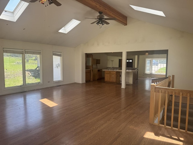 unfurnished living room featuring beamed ceiling, high vaulted ceiling, a ceiling fan, dark wood finished floors, and a skylight