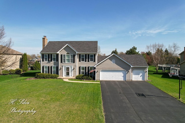 colonial house with an attached garage, a chimney, asphalt driveway, a front yard, and an outdoor structure