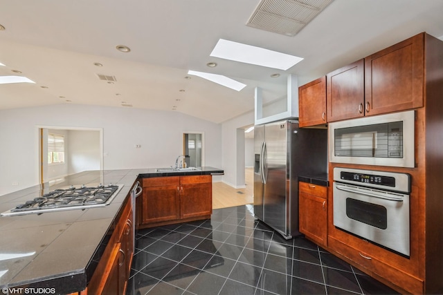 kitchen featuring dark tile patterned floors, visible vents, a sink, lofted ceiling with skylight, and stainless steel appliances