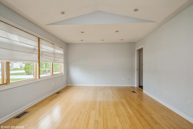 empty room featuring visible vents, baseboards, vaulted ceiling, and light wood-type flooring