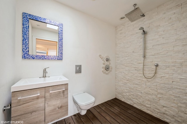 bathroom featuring toilet, a tile shower, wood finished floors, and vanity