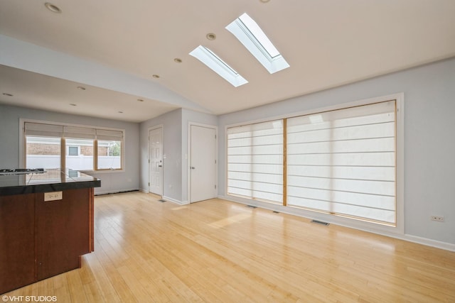 unfurnished living room with visible vents, light wood finished floors, baseboards, and vaulted ceiling with skylight