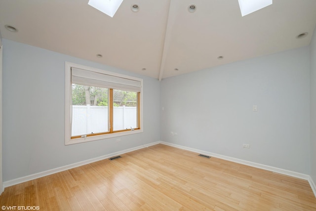 unfurnished room featuring vaulted ceiling with skylight, baseboards, light wood-style flooring, and visible vents