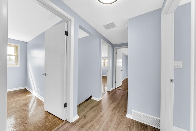 corridor with wood finished floors, visible vents, and baseboards