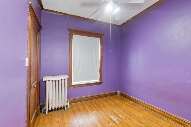 empty room with crown molding, a ceiling fan, radiator heating unit, baseboards, and wood finished floors