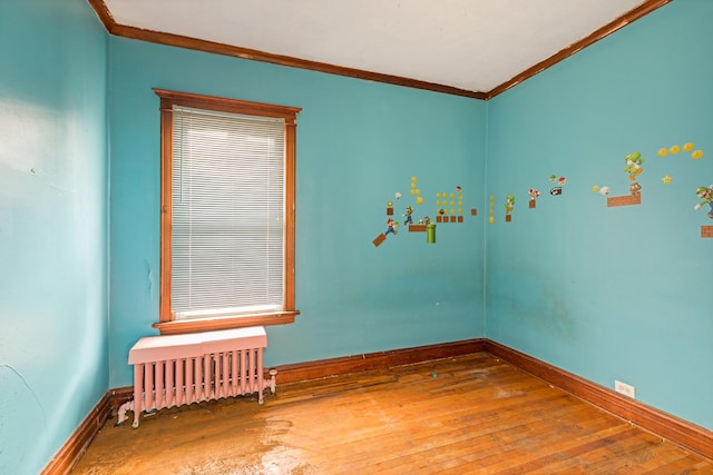 empty room featuring ornamental molding, hardwood / wood-style floors, radiator heating unit, and baseboards