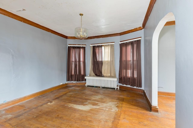 spare room featuring radiator, baseboards, ornamental molding, arched walkways, and wood finished floors
