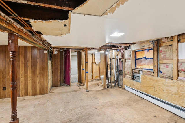 unfinished basement featuring a baseboard heating unit and wooden walls
