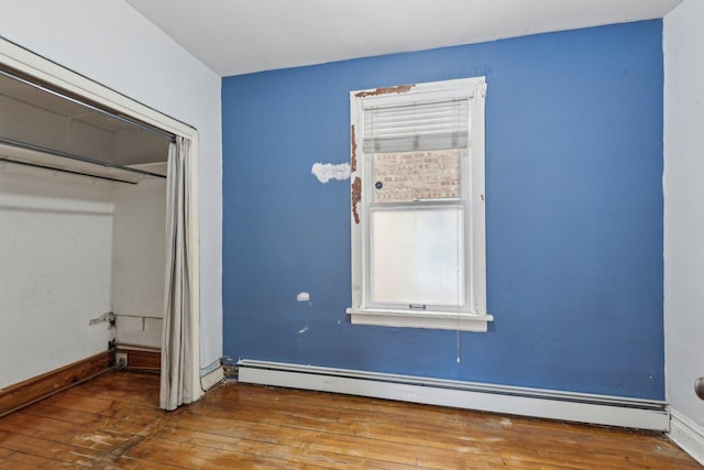 unfurnished bedroom with wood-type flooring, baseboard heating, and baseboards
