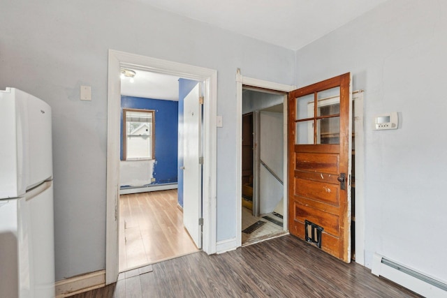 unfurnished bedroom featuring freestanding refrigerator, a baseboard heating unit, wood finished floors, and baseboards