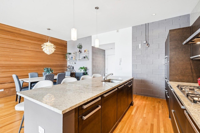 kitchen featuring stainless steel gas stovetop, an island with sink, a sink, light wood-type flooring, and a breakfast bar area