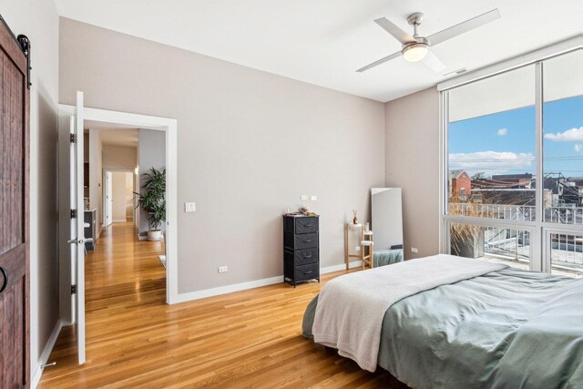 bedroom with a barn door, a ceiling fan, a wall of windows, baseboards, and light wood-style flooring