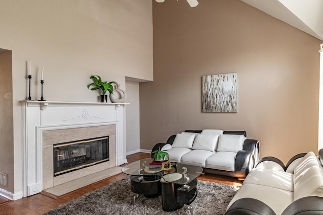 living area with baseboards, wood finished floors, ceiling fan, a premium fireplace, and high vaulted ceiling
