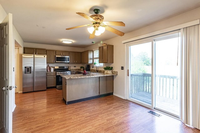 kitchen featuring appliances with stainless steel finishes, a peninsula, a sink, light wood-type flooring, and ceiling fan
