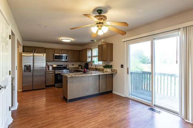 kitchen featuring stainless steel appliances, a peninsula, a sink, wood finished floors, and ceiling fan