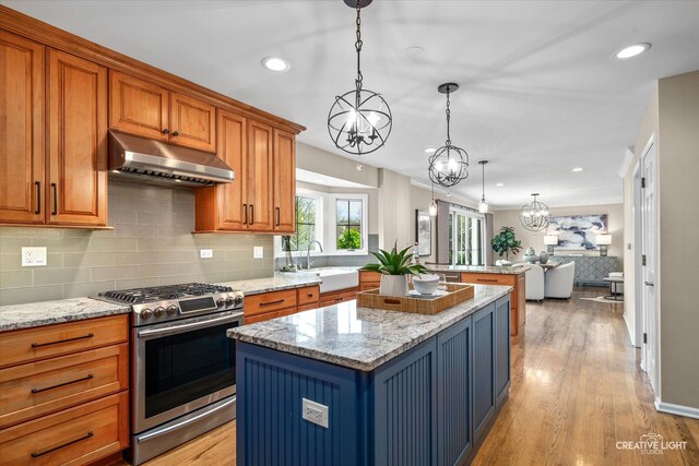 kitchen with an inviting chandelier, a sink, stainless steel range with gas stovetop, under cabinet range hood, and a kitchen island