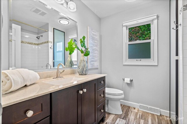 full bath featuring a tile shower, toilet, baseboards, wood finished floors, and visible vents