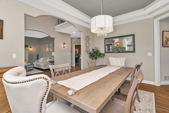 dining area featuring a chandelier, visible vents, baseboards, arched walkways, and wood finished floors