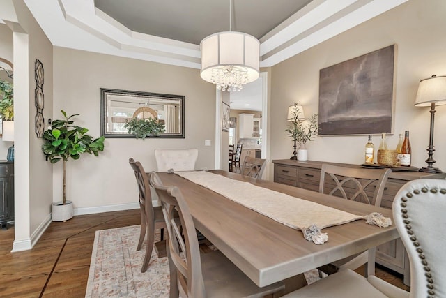 dining space featuring baseboards, wood finished floors, a chandelier, and a raised ceiling