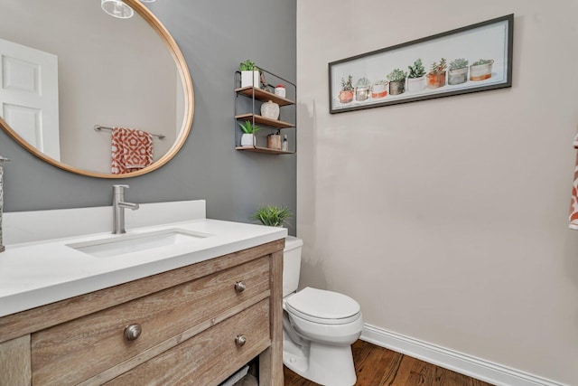 half bathroom featuring toilet, vanity, wood finished floors, and baseboards